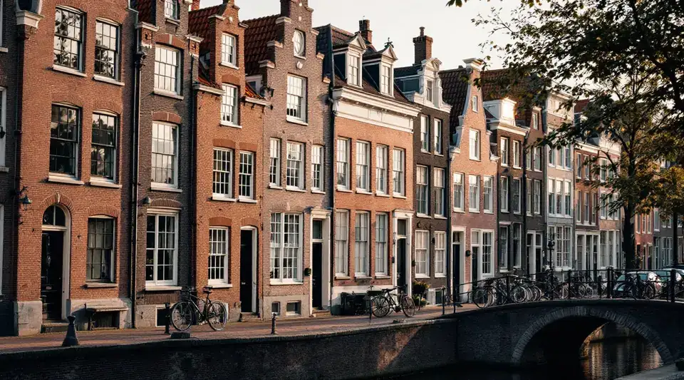 Een rij oude grachtenpanden met smalle bakstenen gevels aan een gracht met fietsen op de brug